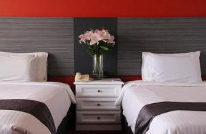 a bedroom with two beds and a vase with pink flowers at Grand Riverview Hotel in Kota Bharu