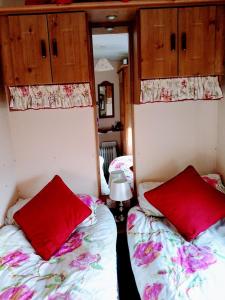 twee bedden in een kamer met rode kussens erop bij Cosy Cottage Caravan in Ashington