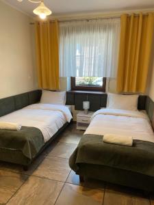 two beds in a room with yellow curtains and a window at Apartamenty Jaskinia Solna in Ruda Śląska