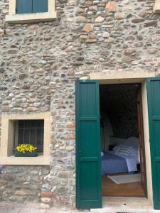 uma cama num edifício de pedra com portas verdes e uma janela em La Guarnigione em Valeggio sul Mincio