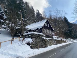 uma cabana de madeira ao lado de uma estrada coberta de neve em Roubenka Dolní Rokytnice em Rokytnice nad Jizerou