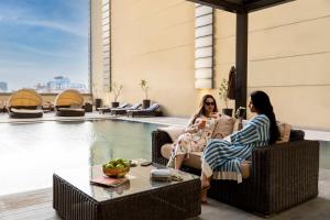 two women sitting on chairs next to a pool at Adagio Aparthotel Jeddah Malik Road in Jeddah