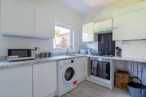 a white kitchen with a washing machine and a microwave at The Sailsbury Snug in Southend-on-Sea