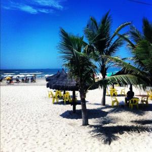 a beach with tables and chairs and palm trees at Apartamento amplo próximo a praia - Faça tudo a pé in Guarujá