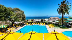 a large swimming pool with yellow chairs and the ocean at Hôtel LES MIMOSAS TABARKA in Tabarka