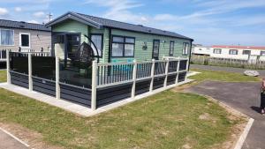 a green tiny house with a white railing at 17 Wildflower Meadow in Chapel Saint Leonards