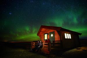 a couple of people standing outside of a cabin under the northern lights at Mid Hvoll Cottages in Suður Hvoll