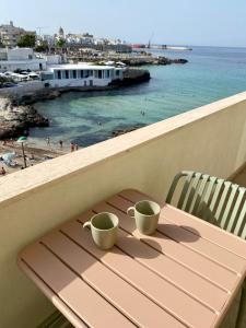 two coffee cups sitting on a wooden table on the beach at La Vue est Belle - Puglia Mia Apartments in Monopoli