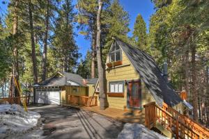 a small yellow house with a wooden deck in the woods at Lakes Edge Lodge A-frame steps away from the lake! in Lake Arrowhead
