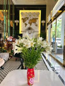 Thành Nam Hotel Tuần Châu في ها لونغ: مزهرية حمراء مليئة بالورود البيضاء على طاولة