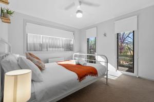 a bedroom with a white bed with an orange blanket on it at The Oasis of Calm by Experience Jervis Bay in Huskisson