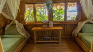 a room with two beds and a table and windows at Elang Hillside Bamboo Villas in Labuan Bajo