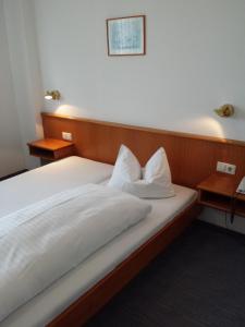 ein Bett mit weißer Bettwäsche und Kissen darauf in der Unterkunft Hotel am Exerzierplatz in Mannheim