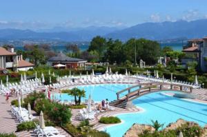 a large swimming pool with white chairs and a bridge at Claudia House Green Residence Sirmione in Desenzano del Garda