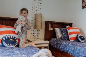 a child sitting on a bed holding a teddy bear at Captain John's River House in Goolwa North