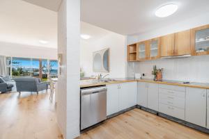 a kitchen with white cabinets and a living room at Quarterdeck Unit 2 - Lennox Head in Lennox Head
