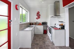 a kitchen with white cabinets and a red door at Tyne and Tides in Oamaru