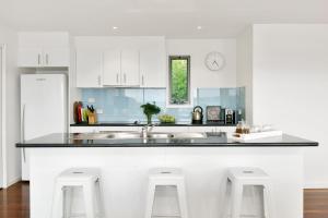 a kitchen with white cabinets and a counter with stools at Scelta in Lorne +12 photos
