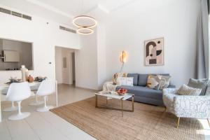 The Smart Concierge - Sandoval Gardens JVC في دبي: غرفة معيشة مع أريكة زرقاء وكراسي بيضاء
