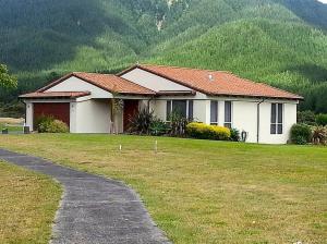 una casa blanca con un patio de hierba frente a una montaña en Mistry Hideout - Lakes Resort Pauanui Home, en Pauanui