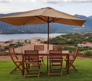 een houten tafel met stoelen en een parasol bij Appartement neuf 3 chambres vue mer Propriano in Propriano