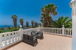 a white fence and benches on a balcony with palm trees at Gorgeous Golf Villa Heated Pool Sea view in Adeje