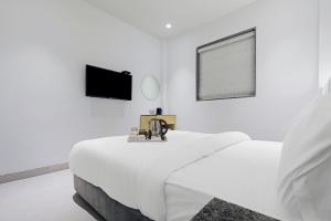 a white bedroom with a bed and a flat screen tv at FabHotel Yellow Courtyard in Bhopal