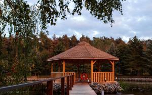 a wooden gazebo in a park next to a pond at ERNESTÓWKA - Hotel in Czarna