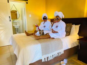 two women in white robes sitting on a bed at Mrhali Boutique Guest House in Kwamhlanga