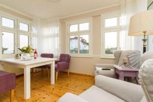 uma sala de estar com uma mesa, cadeiras e janelas em Villa Albertine App 08 em Ahlbeck