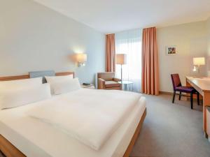 a hotel room with a large white bed and a desk at Mercure Hannover Oldenburger Allee in Hannover