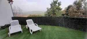 zwei weiße Stühle auf einem Rasen mit einem Zaun in der Unterkunft La puerta el sol in Villanueva del Conde