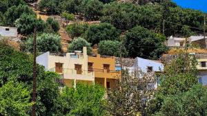 a yellow building on top of a hill with trees at Cinnamon House in Kritsa in Kritsá