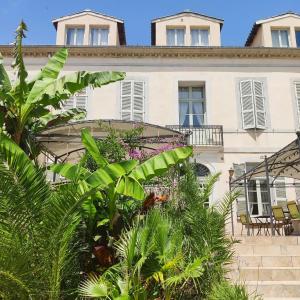 een groot wit gebouw met planten ervoor bij Chambres d'hôtes - Bed and Breakfast Les Palmiers in Mèze