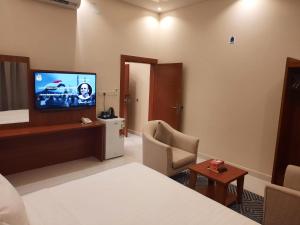 Cette chambre comprend un lit, une télévision et une chaise. dans l'établissement المهيدب للوحدات السكنية, à Buraydah