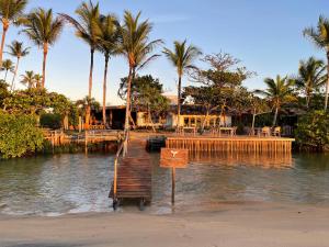 a dock in the water with a house and palm trees at Hotel Calá & Divino in Praia do Espelho
