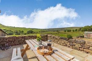 a wooden picnic table on a patio with a stone wall at Jim's Barn in Diggle