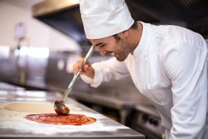 海上米蘭的住宿－Hotel Elefantino Grey - Inclusi Colazione & Brunch fino alle 13-00 - Vicinissimi a Mirabilandia，厨师正在准备一张餐桌上的比萨饼