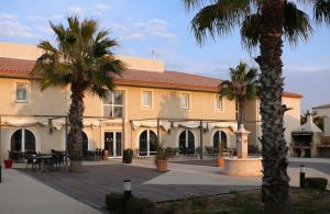 a building with palm trees in front of it at Hôtel Jasses de Camargue in Gallargues-Le-Montueux