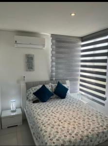 a bedroom with a bed with blue pillows and a window at Apartamento - Velas al Mar, Santa Marta in Gaira