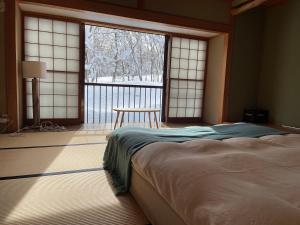 a bedroom with a bed and a window and a table at Myoko Woodland Lodge in Myoko