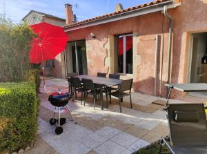 a table and chairs with a red umbrella and a grill at Gîte Le Petit Bambou in Bressuire +3 photos