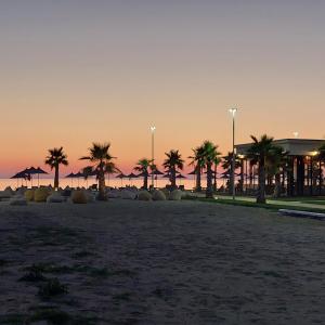 a beach with palm trees and umbrellas at sunset at Vala Mar apartment- A41 in Durrës