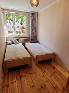 two beds in a room with a window and wooden floors at Apartament 5 minut spacerem od plaży in Giżycko