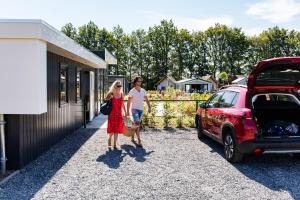 un hombre y una mujer caminando junto a un coche rojo en EuroParcs Limburg, en Susteren