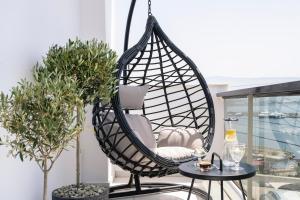 a hanging rattan swing chair on a balcony with two tables at Divine Residence, a SeaView Retreat, By ThinkVilla in Piraeus