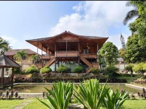 een groot houten huis met een vijver ervoor bij The Kulawi Villa & Resort in Puncak