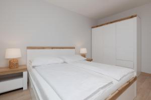 a white bedroom with a large bed and a window at Jantar Apartamenty Siedem Wysp in Sianozety