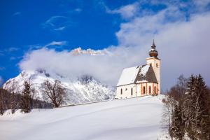 eine Kirche auf einem schneebedeckten Hügel mit einem Berg im Hintergrund in der Unterkunft Portis Appartements in Dienten am Hochkönig