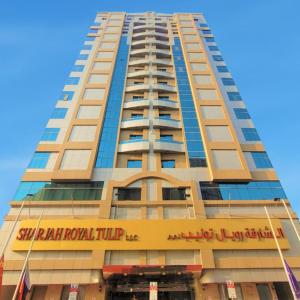 a tall building with a sign for a hotel at Sharjah Royal Tulip Hotel Apartments توليب رويال الشارقة in Sharjah
